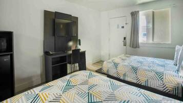 A hotel room with two beds, a TV, a wardrobe, and a window with curtains.