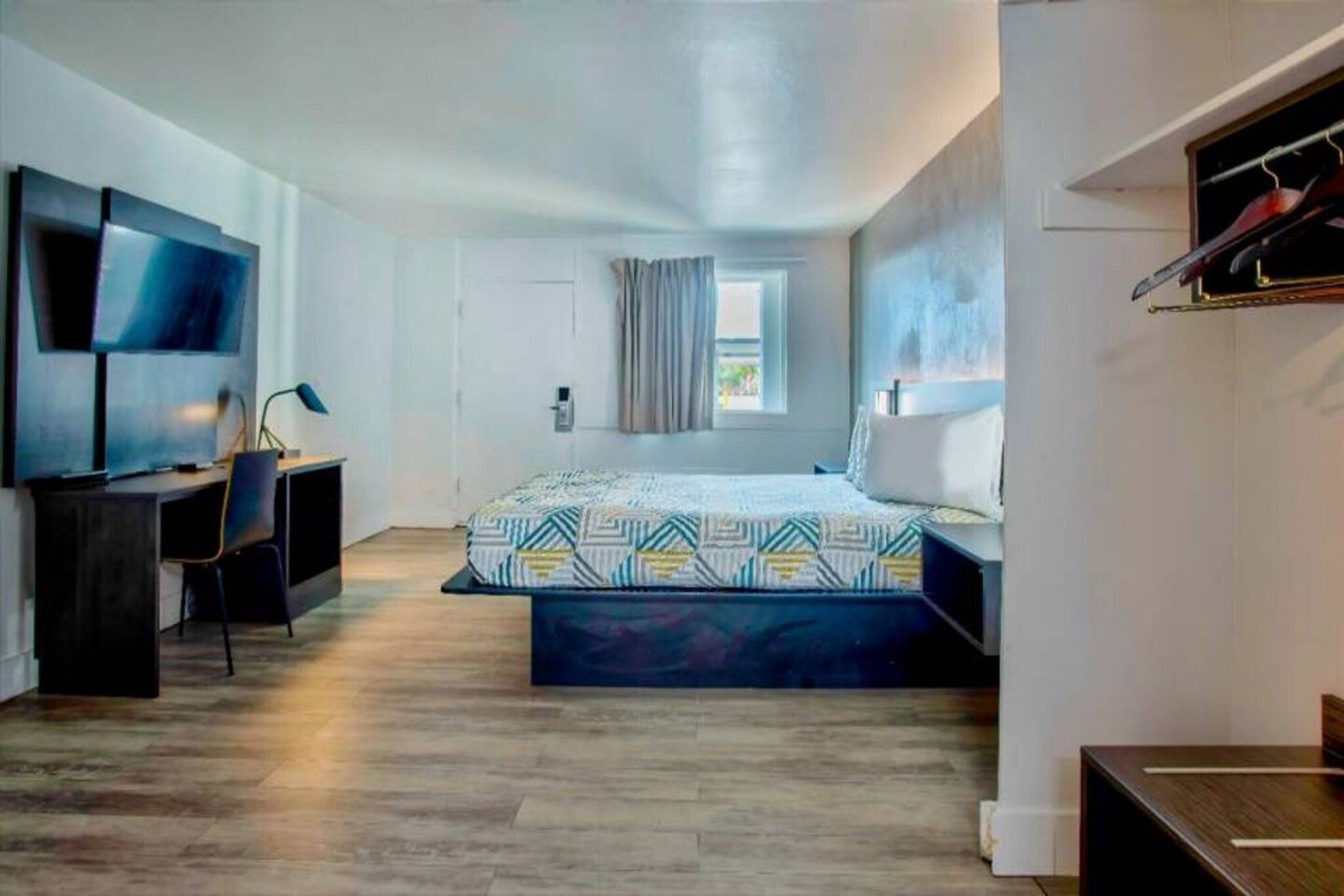A modern hotel room with a bed, a desk, a TV, and a window.