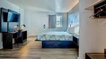 A modern hotel room with a bed, a desk, a TV, and a window.
