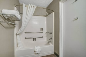 Un baño con ducha a nivel, barras de apoyo y un perchero para toallas.