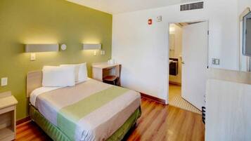 A hotel room with a bed, bedside tables, a chair, a desk, and a television.