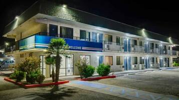 A multi-story hotel with a blue 'WELCOME' sign, multiple balconies, and a parking lot.