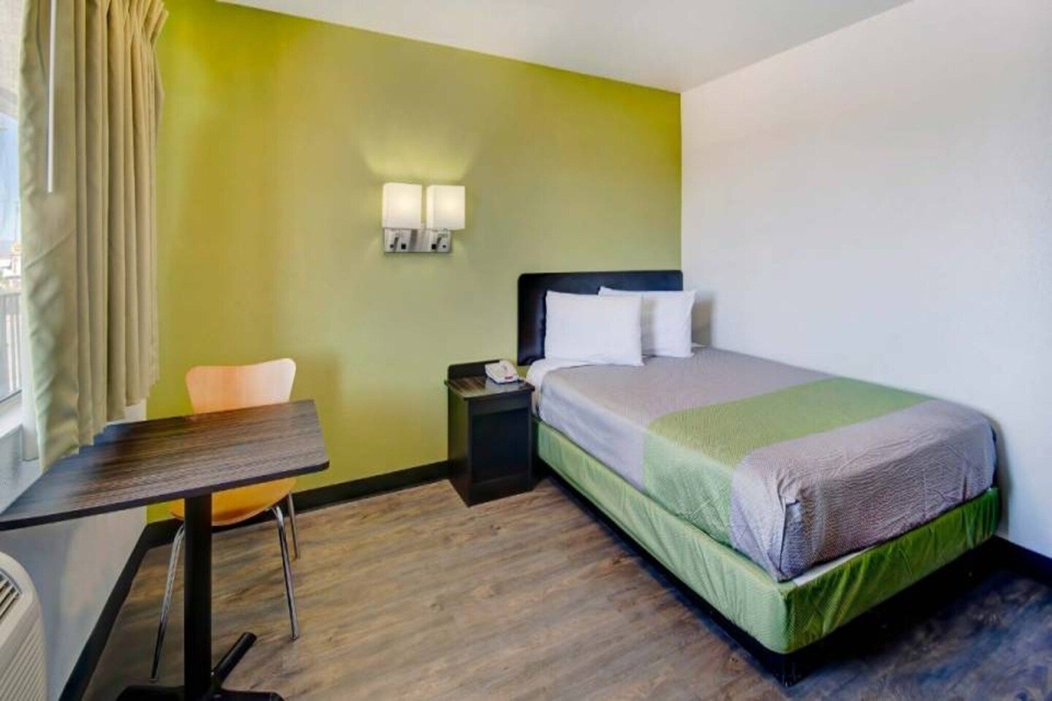 A hotel room with a bed, bedside table, chair, and a desk with a chair.