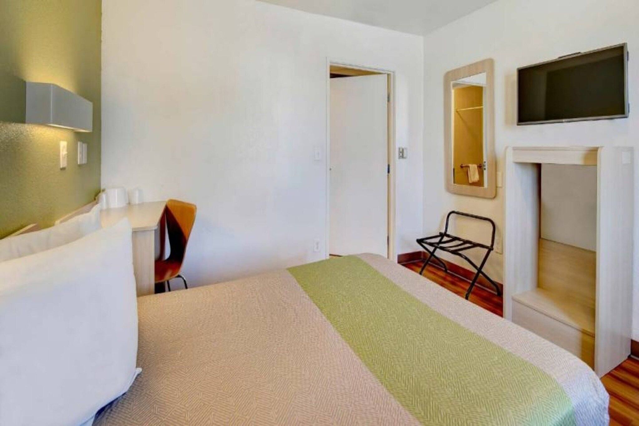 Ett hotellrum med en säng, en stol, en tv och en spegel.