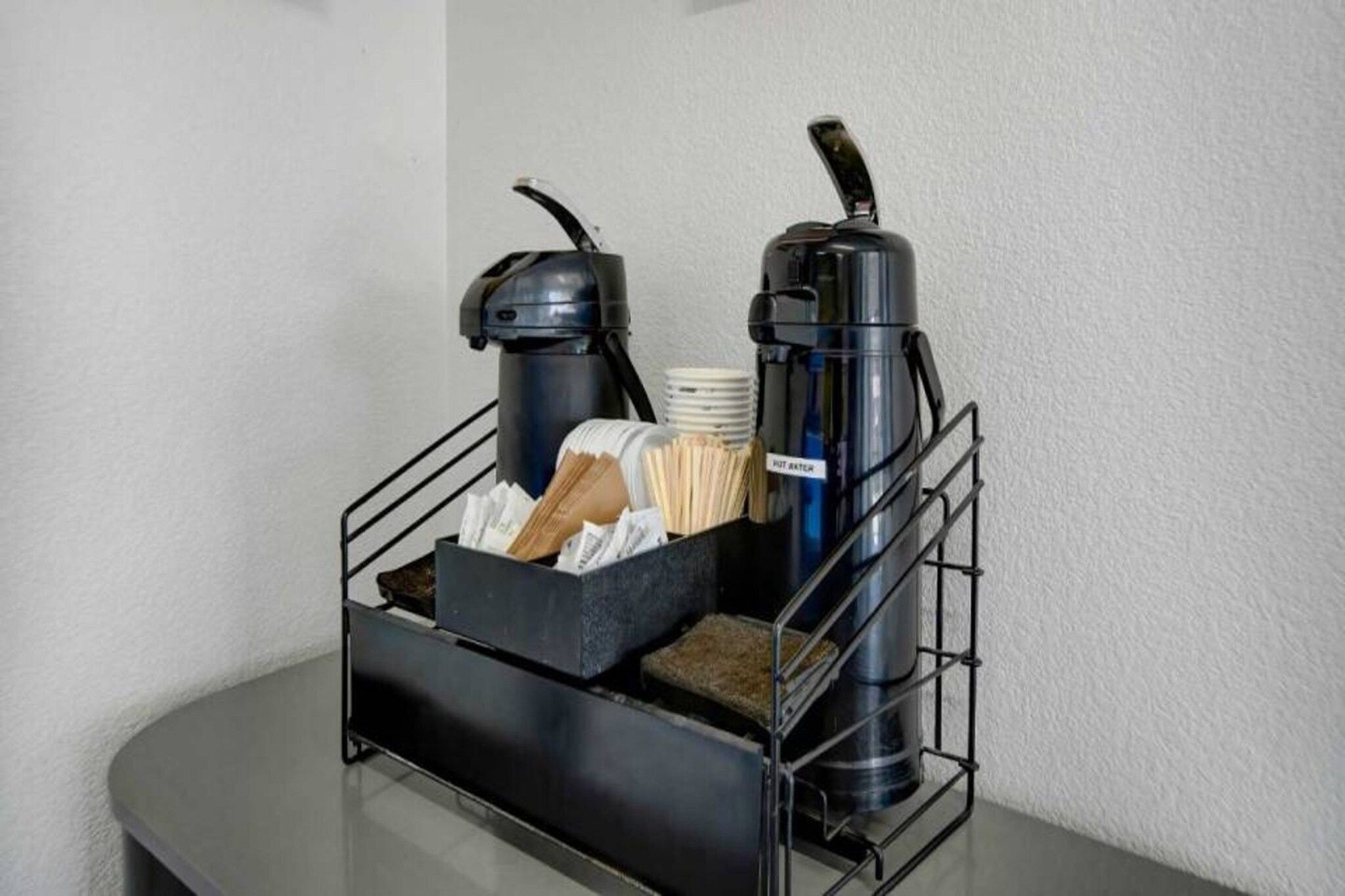 Un présentoir métallique pour le café, comprenant une machine à café, un thermos et une boîte contenant des serviettes en papier et des mouchoirs.
