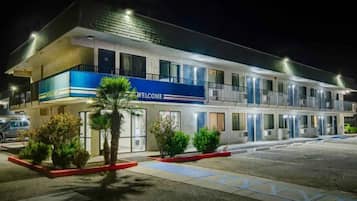 A multi-story hotel with a blue 'WELCOME' sign, multiple balconies, and a parking lot.