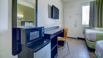 A hotel room with a bed, a desk with a microwave, a chair, a television, and a window with curtains.