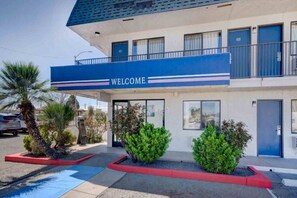 Un motel con un letrero que dice 'WELCOME', un estacionamiento y una palmera.