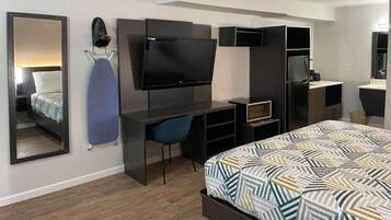 A modern hotel room with a bed, a desk with a flat-screen TV, a chair, and a mirror.