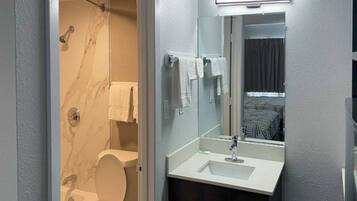 A bathroom with a toilet, a shower, a sink, and a mirror.