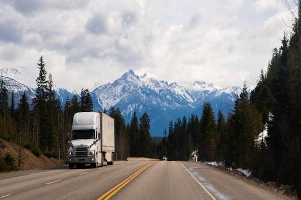 A road with a large truck and a smaller vehicle, surrounded by snow-capped mountains and dense forests. - 2 Full Beds | Non-Smoking, Kitchen (Vicksburg MS)