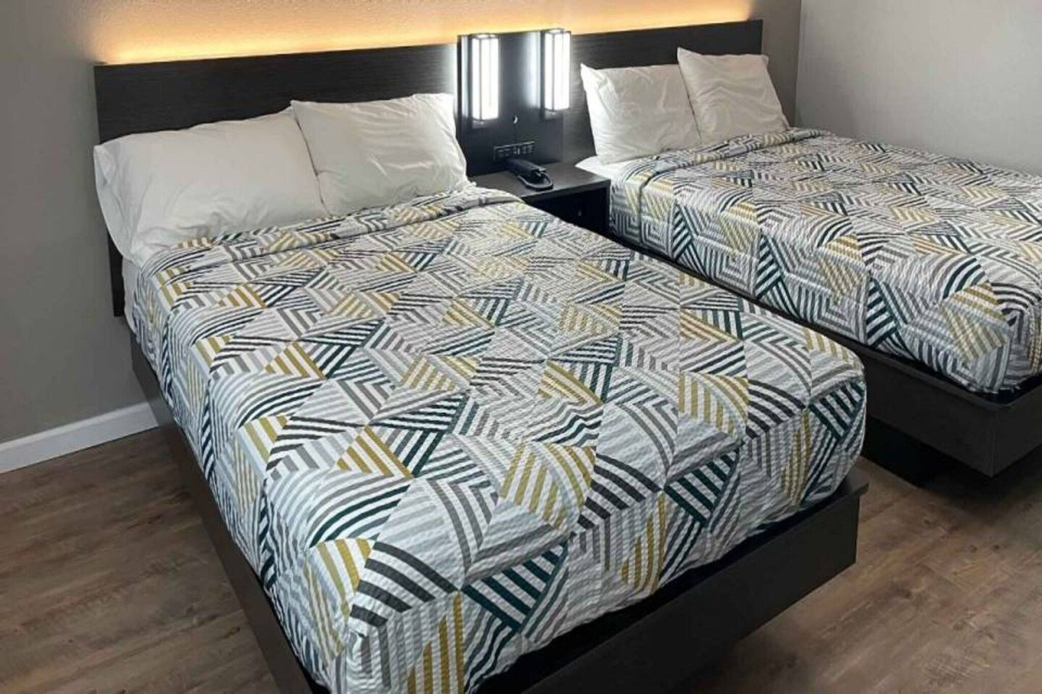 A hotel room with two beds, each with patterned bedding, a bedside table with a lamp, and a headboard.