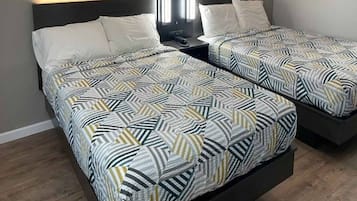 A hotel room with two beds, each with patterned bedding, a bedside table with a lamp, and a headboard.