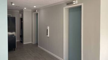 A hallway with a grey wall, a door with a blue handle, and a stainless steel appliance on the left.