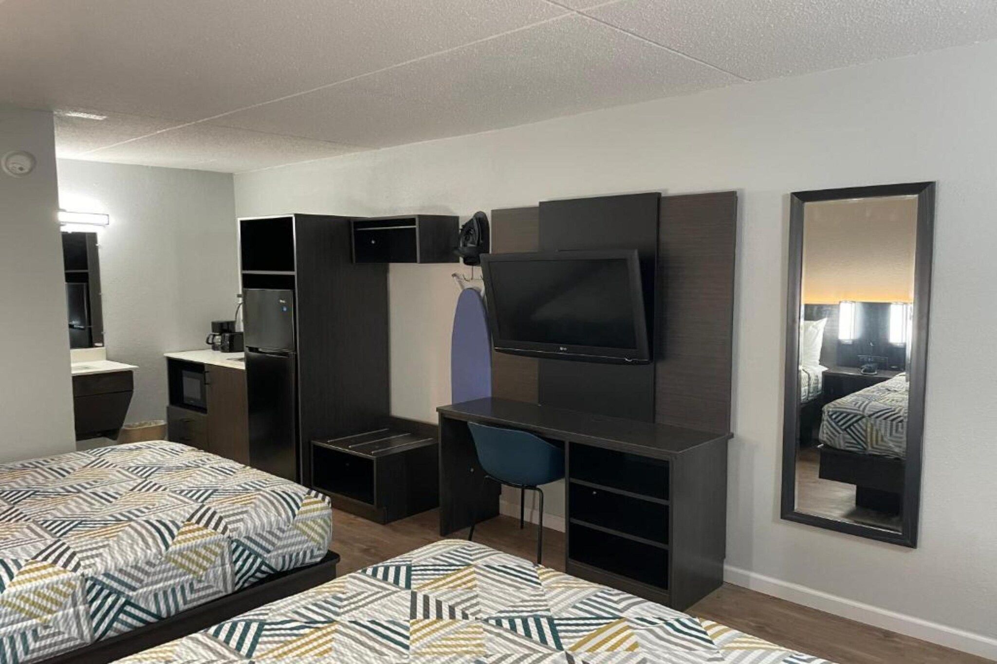 A hotel room with two beds, a desk, a TV, and a mirror.