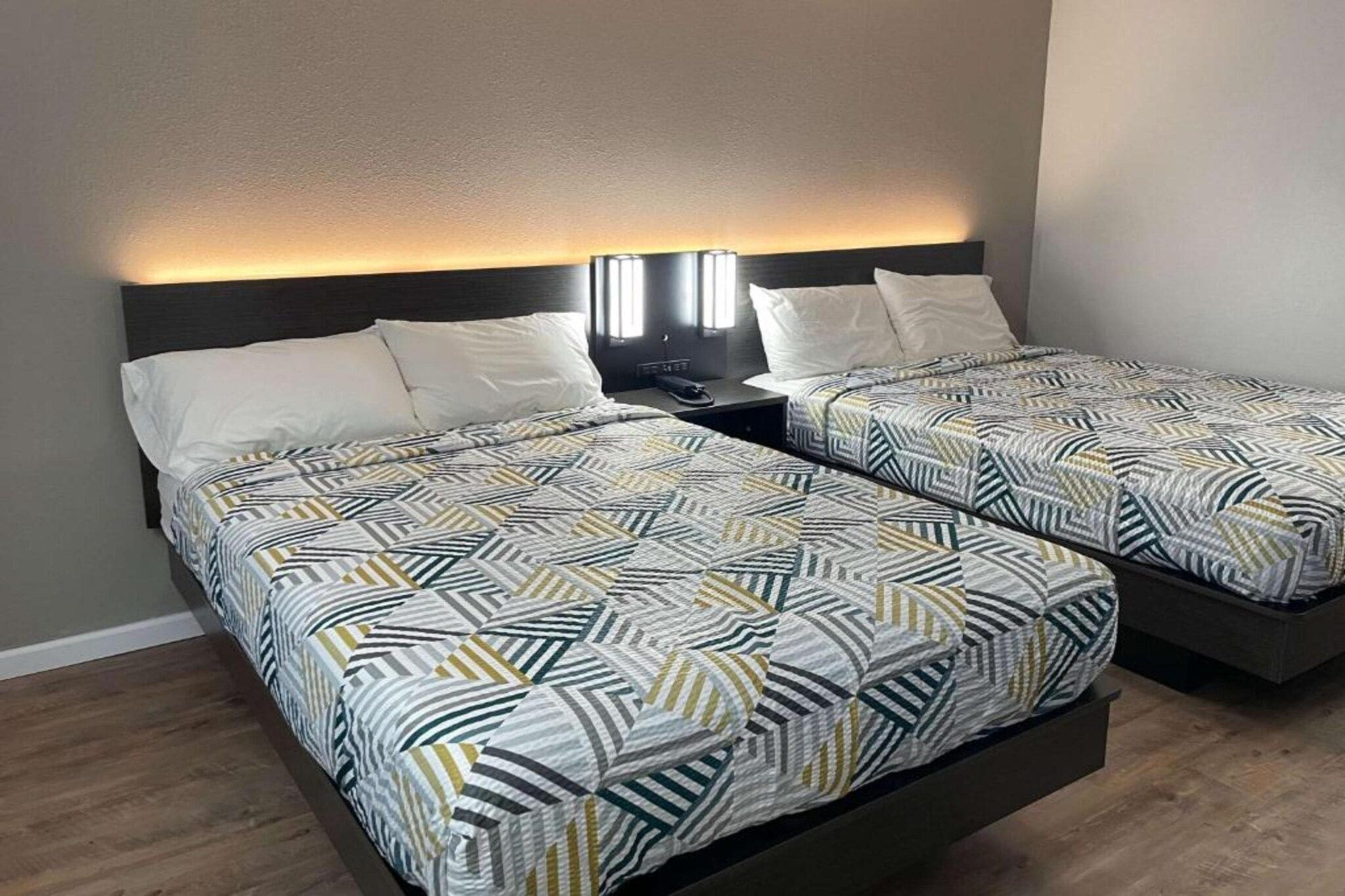 Een tweepersoonskamer met twee bedden, elk met een bedovertrek met een patroon, een nachtkastje met een lamp en een hoofdbord met ingebouwde verlichting.