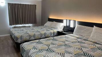 A hotel room with two beds, each with patterned bedding, a nightstand, and a wall-mounted lamp.