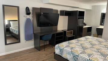 Quarto moderno com cama, televisão, escrivaninha e espelho.