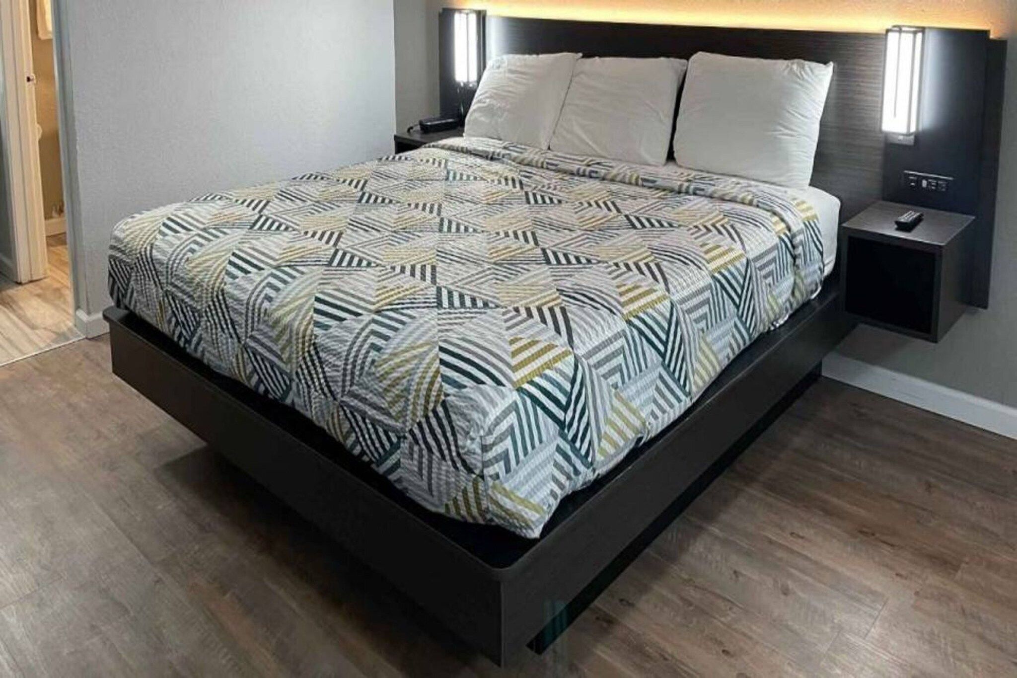 A modern bed with a geometric patterned bedspread, a dark headboard, and bedside lamps.