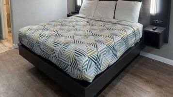 A modern bed with a geometric patterned bedspread, a dark headboard, and bedside lamps.