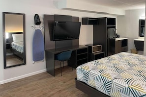 Quarto de hotel moderno com uma cama, uma escrivaninha com televisão de tela plana, uma cadeira e um espelho.