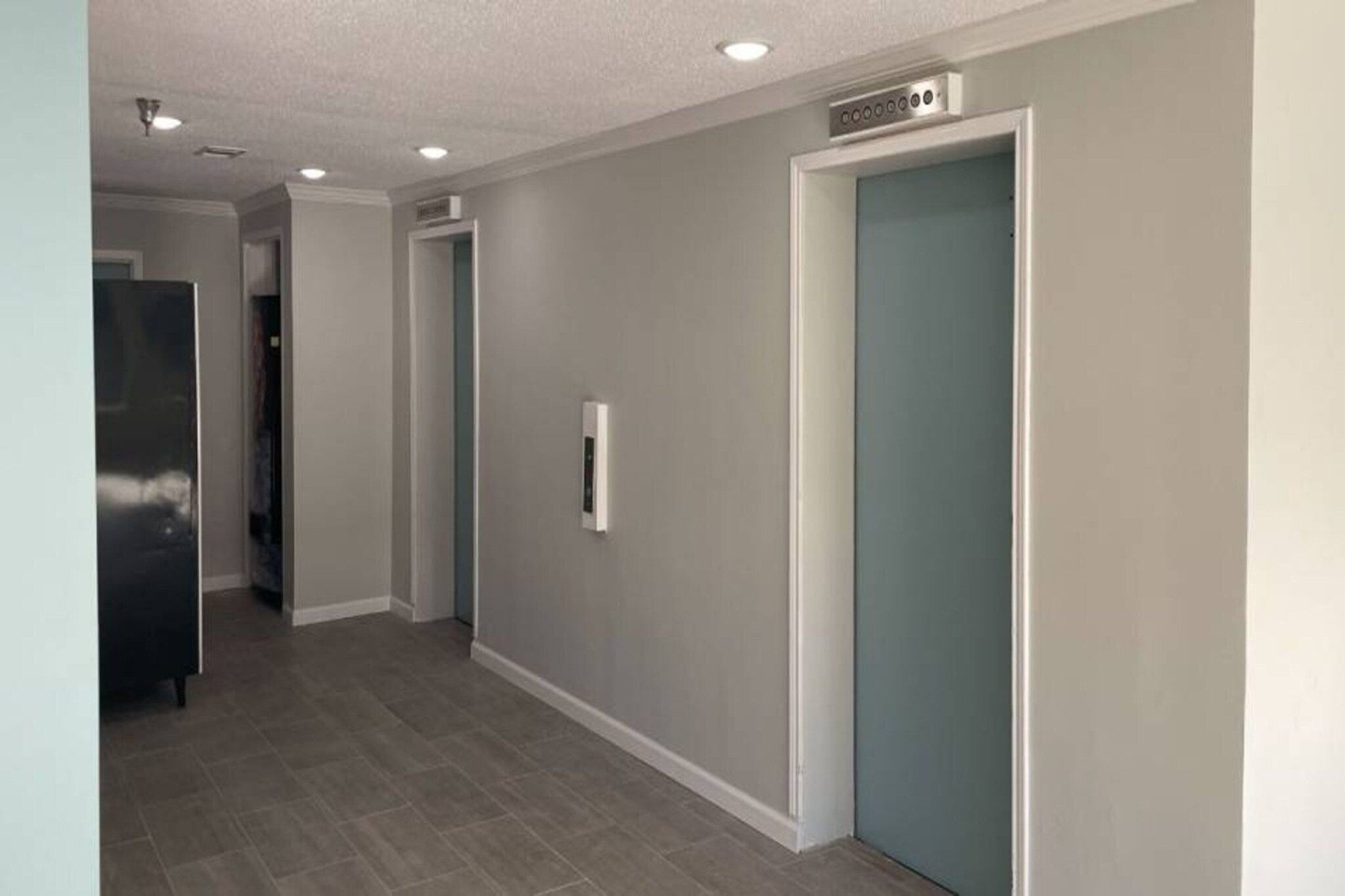 A hallway with a grey wall, a door with a blue handle, and a stainless steel appliance on the left.