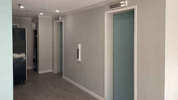 A hallway with a grey wall, a door with a blue handle, and a stainless steel appliance on the left.