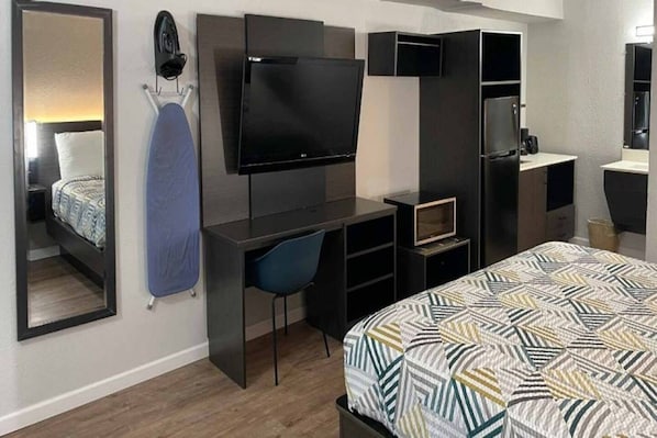 A hotel room with a bed, a desk with a chair, a television, a wardrobe, and a mirror.