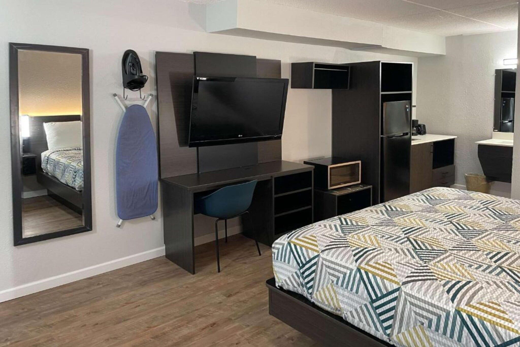 A modern hotel room with a bed, a desk with a flat-screen TV, a chair, and a mirror.