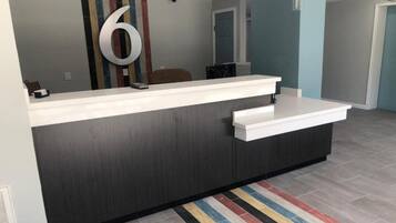 A reception desk with a large number '6' on the wall, a modern design with a dark wood finish, and a striped rug on the floor.