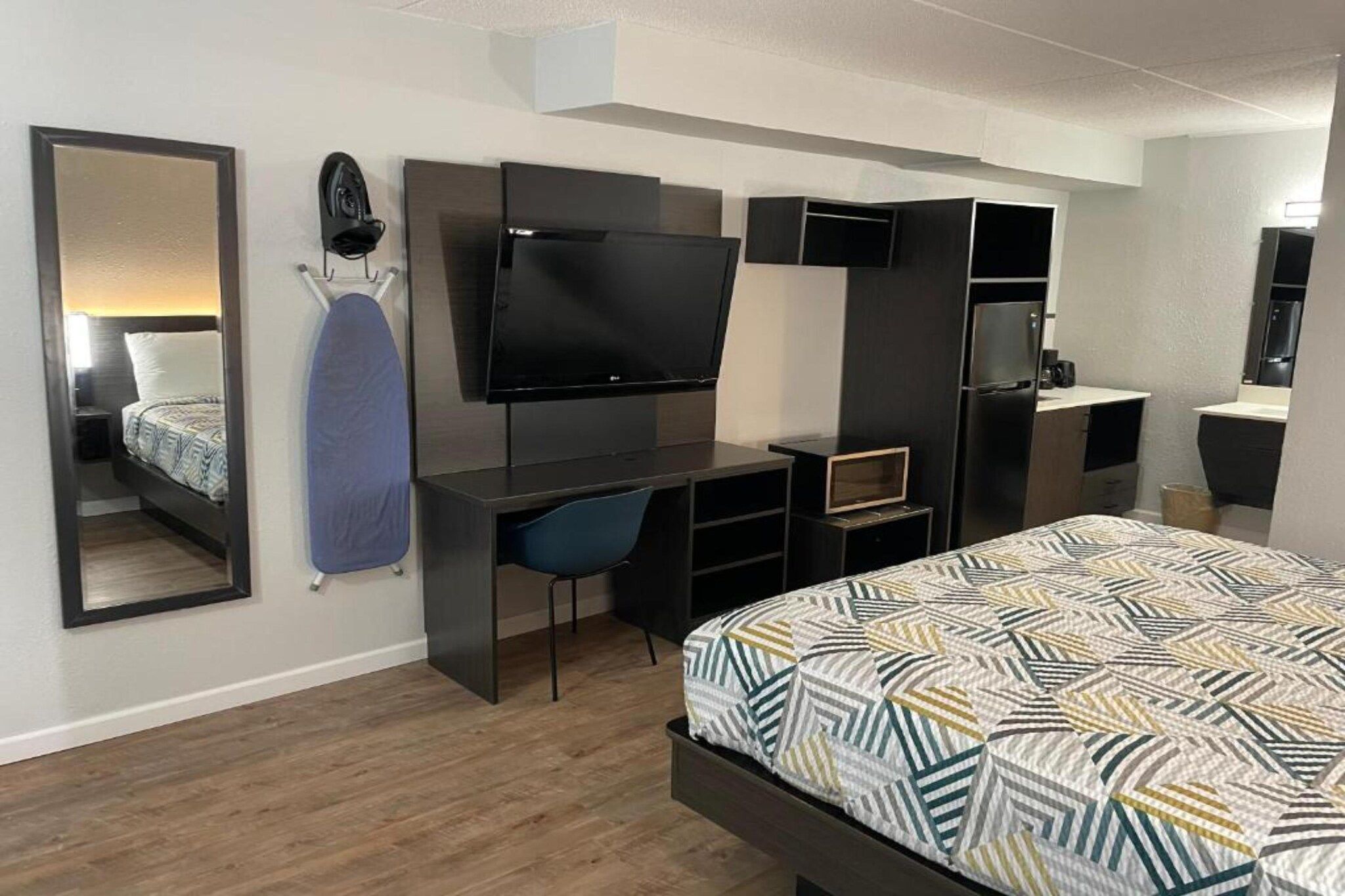 Ein modernes Schlafzimmer mit einem Bett, einem Fernseher, einem Schreibtisch und einem Spiegel.