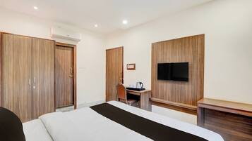 Quarto de hotel com uma cama, uma secretária com cadeira, televisão fixada na parede e um guarda-roupa.