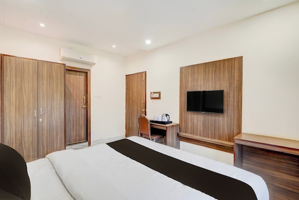 A hotel room with a bed, a desk with a chair, a television mounted on the wall, and a wardrobe. - OYO Townhouse Prayagraj (Prayagraj)