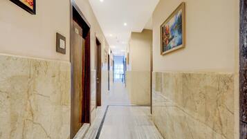 A hallway with marble flooring, doors, and framed artwork on the walls.