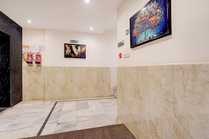 Un hall d’entrée aux murs de marbre, un extincteur, un panneau indiquant la sortie de secours et un panneau indiquant le deuxième étage.