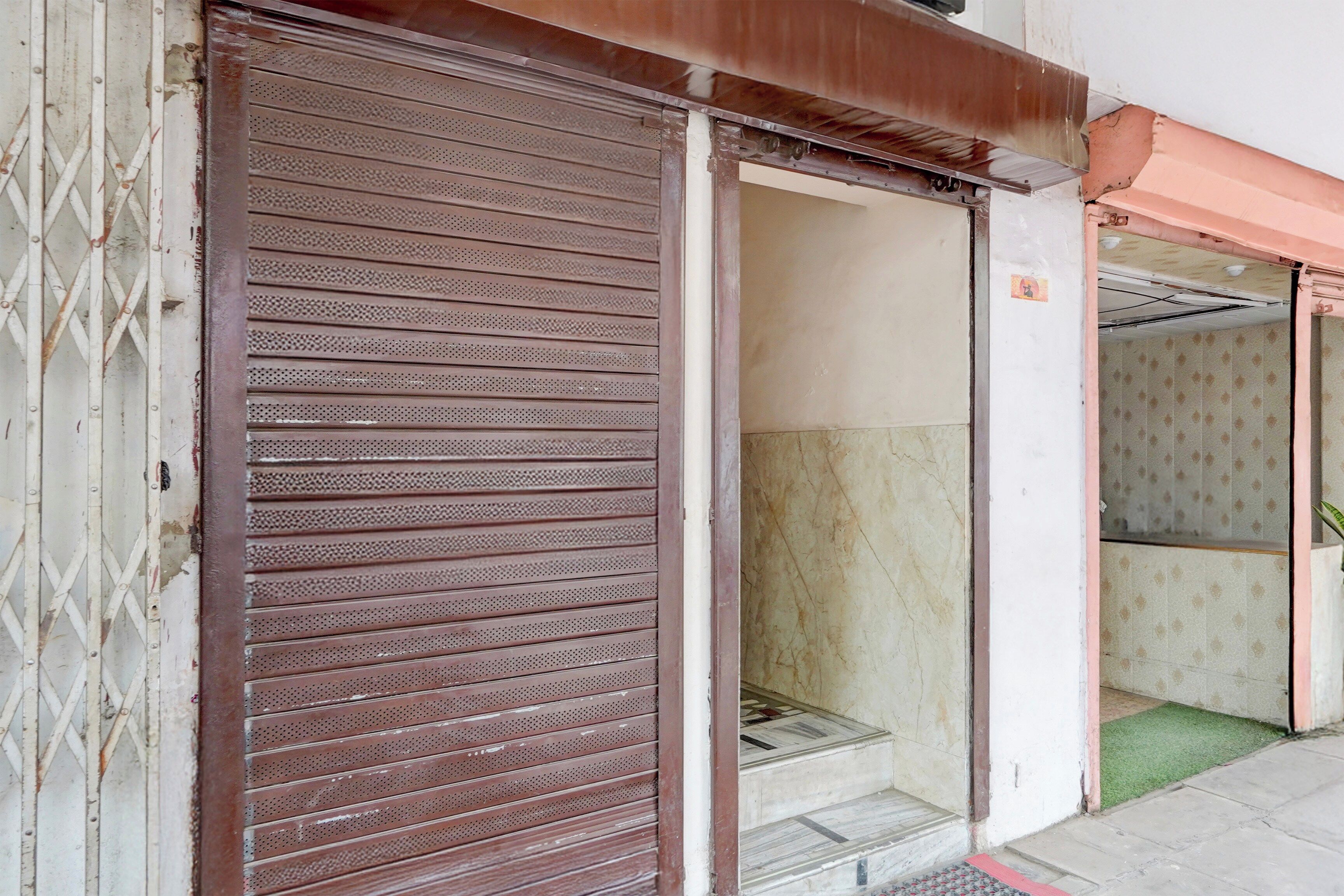 A closed metal shutter door with a patterned design, a visible threshold, and a tiled floor leading to a staircase.