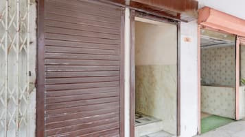 A closed metal shutter door with a patterned design, a visible threshold, and a tiled floor leading to a staircase.