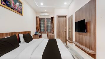 A hotel room with a bed, a TV, a desk, and a window with curtains.