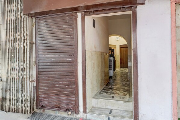 A closed metal gate with a padlock, a tiled entrance, and a hallway leading to a room with a clock on the wall.