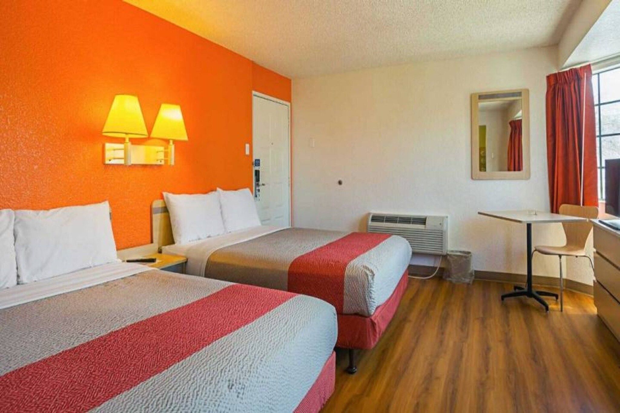 Une chambre d’hôtel avec deux lits, un bureau, une chaise, un miroir et une fenêtre avec des rideaux.