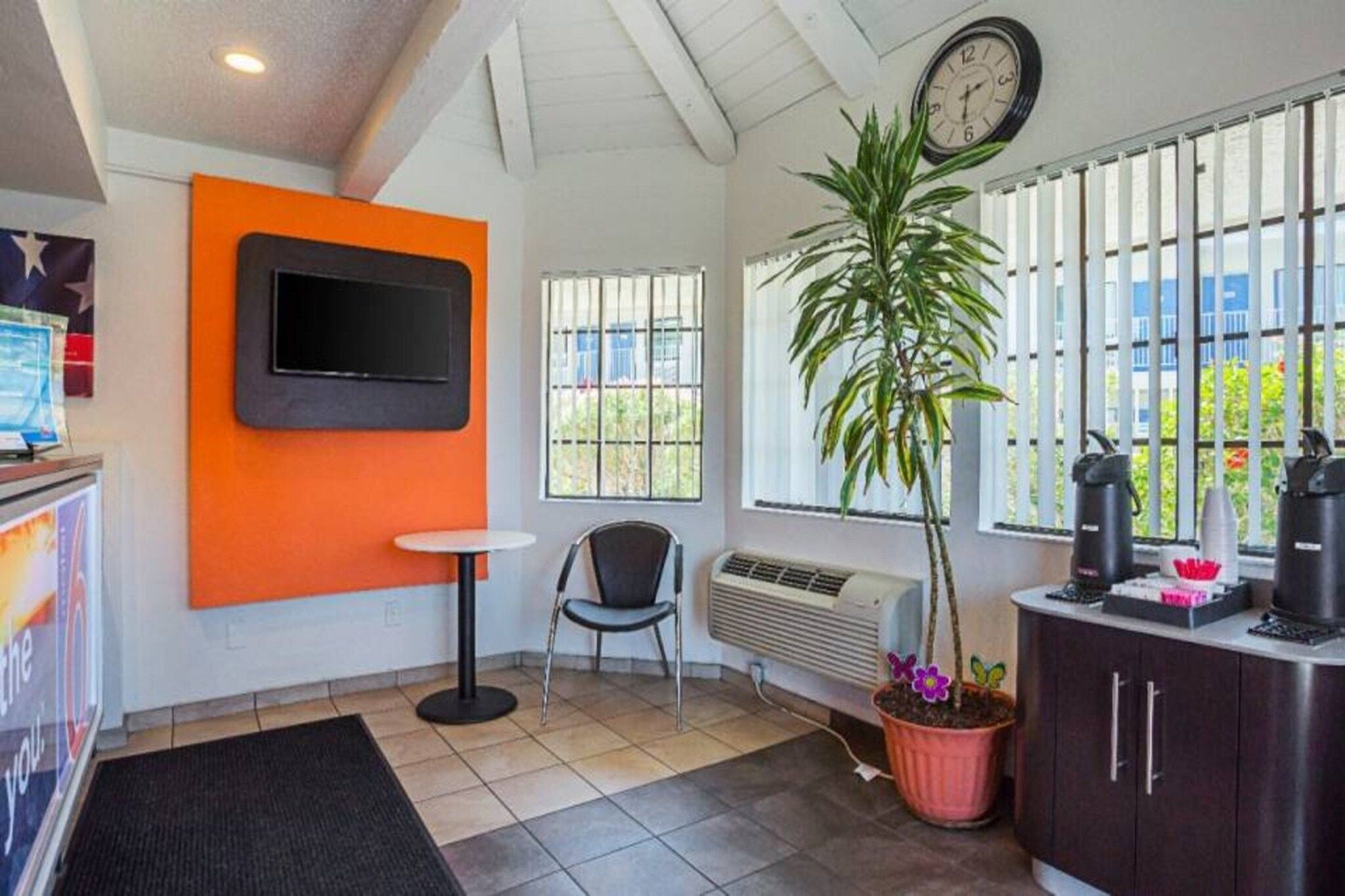 Une pièce avec un téléviseur fixé au mur orange, une chaise, une plante en pot, un radiateur et une fenêtre avec des stores.