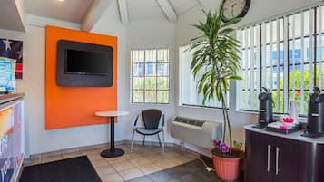 Une pièce avec un téléviseur fixé au mur orange, une chaise, une plante en pot, un radiateur et une fenêtre avec des stores.