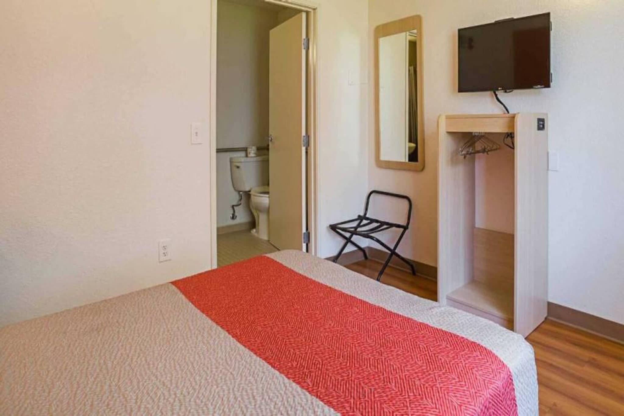 Une chambre à coucher avec un lit, une chaise, un téléviseur et une salle de bain visible à travers une porte ouverte.