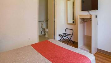 Une chambre à coucher avec un lit, une chaise, un téléviseur et une salle de bain visible à travers une porte ouverte.