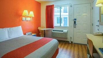 Habitación de hotel con cama, escritorio, silla, ventana con cortinas y puerta.