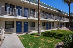 Un motel à deux étages avec des portes bleues, un espace de stationnement couvert et une petite pelouse.