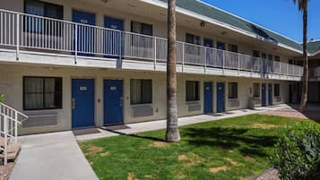 Un motel con una estructura de dos pisos, varias habitaciones con puertas azules y un pequeño jardín.