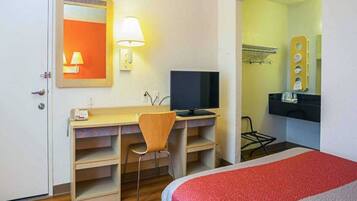 Habitación de hotel con escritorio, silla, televisión y cama con cubrecama rojo y gris.