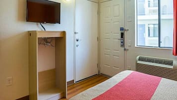Quarto de hotel com cama, televisão na parede, guarda-roupa e janela com vista para edifícios.