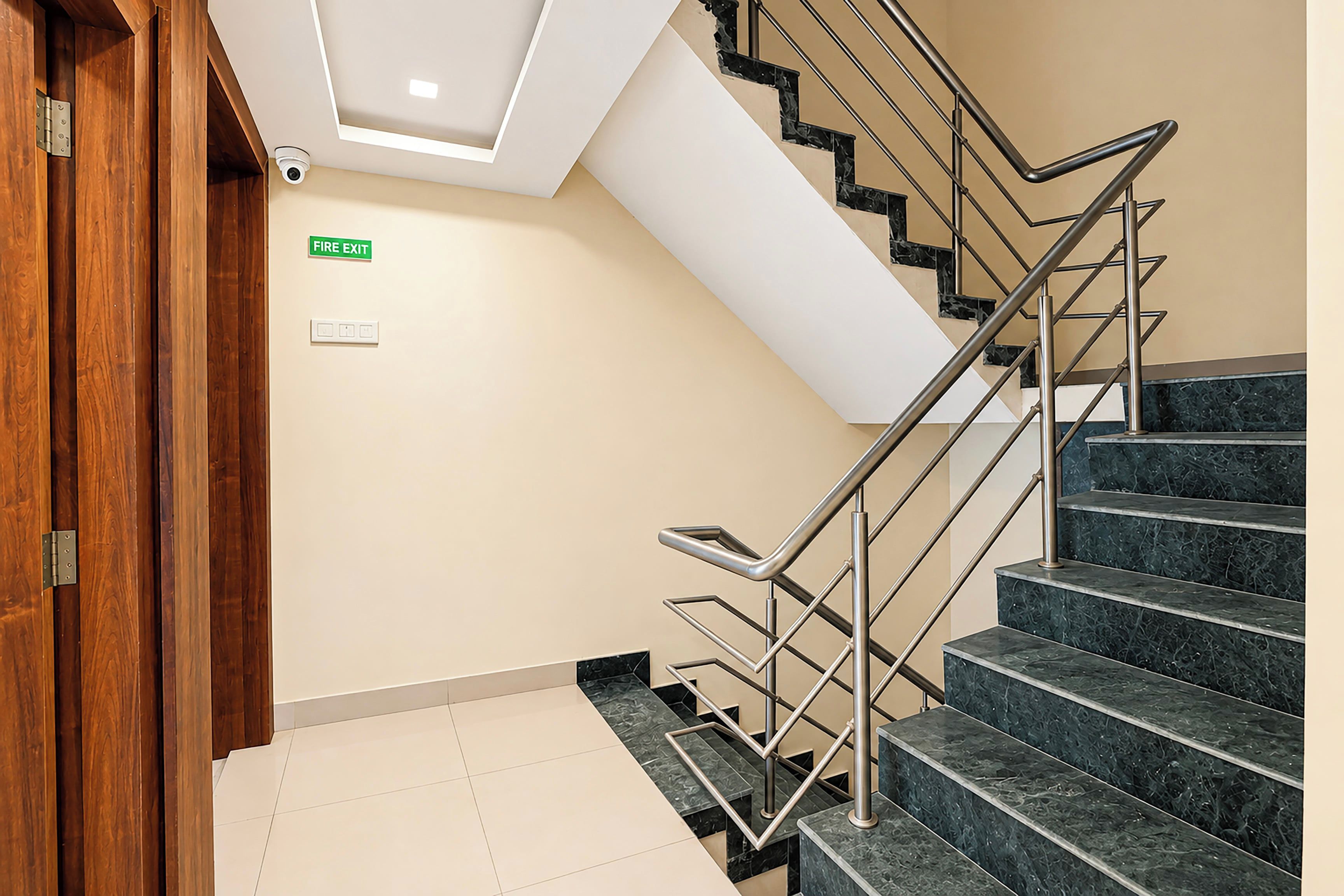 A staircase with a fire exit sign, a security camera, and a wooden door.